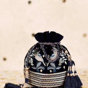 May include: A navy blue velvet drawstring bag with detailed embroidery. The bag showcases a bird and floral design in blue and gold. Gold trim and tassels add a touch of elegance. A stylish accessory for special occasions.