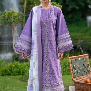 Peut inclure: Une robe lilas à manches longues avec broderies florales et une écharpe assortie. La robe présente une encolure en V et des boutons décoratifs. L'ensemble est associé à un pantalon et des sandales assortis, créant une tenue coordonnée.