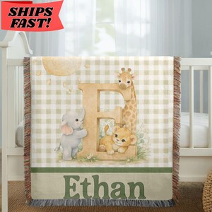 May include: A woven throw blanket featuring a beige and white gingham pattern with a large letter E. The design includes a cartoon elephant, giraffe, and lion cub. The name Ethan is printed in dark green text at the bottom of the blanket.