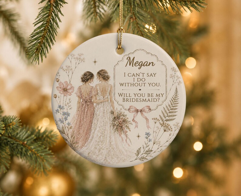 Puede incluir: Un adorno redondo de cer&aacute;mica blanca con una ilustraci&oacute;n de dos figuras con vestidos, uno rosa y otro blanco, rodeados de motivos florales. El texto dice: Megan, I CAN'T SAY I DO WITHOUT YOU. WILL YOU BE MY BRIDESMAID? con un lazo rosa.