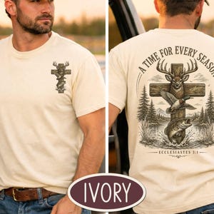 May include: An ivory t-shirt featuring a small graphic on the front left chest and a large graphic on the back. The back design shows a wooden cross with a deer, a duck, and a fish, surrounded by trees and water, with the text A TIME FOR EVERY SEASON and ECCLESIASTES 3:1.
