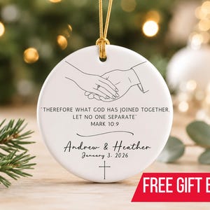 May include: A round white ceramic ornament featuring a black line drawing of two hands holding each other. The text reads: "THEREFORE WHAT GOD HAS JOINED TOGETHER, LET NO ONE SEPARATE" MARK 10:9, "Andrew & Heather", "January 3, 2026", and a cross.