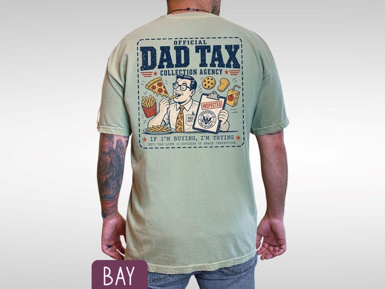 May include: Sage green t-shirt with a graphic on the back that reads "OFFICIAL DAD TAX COLLECTION AGENCY." The graphic features a cartoon man eating pizza and fries. The text "IF I'M BUYING, I'M TRYING" is also included.