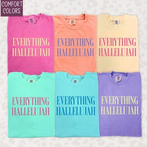 Könnte beinhalten: Sechs Comfort Colors T-Shirts in verschiedenen Farben: Pink, Pfirsich, Gelb, Türkis, Hellblau und Lila. Jedes Shirt trägt den Aufdruck "EVERYTHING HALLELUJAH". Die Shirts sind gefaltet und in einem Raster angeordnet.