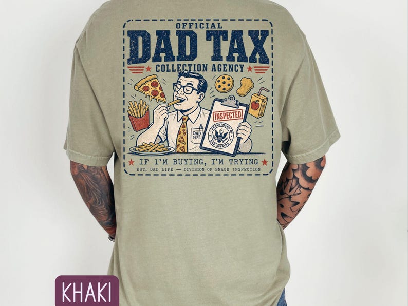 May include: Khaki t-shirt with a graphic on the back. The graphic reads "OFFICIAL DAD TAX COLLECTION AGENCY" and features a cartoon man eating pizza and fries, holding a clipboard with an "INSPECTED" stamp. The text "IF I'M BUYING, I'M TRYING" is also included.