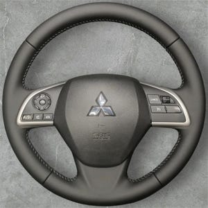 May include: A black leather steering wheel with silver detailing and a Mitsubishi emblem. The wheel has integrated controls and stitching around the rim. The centre features the text "SRS AIRBAG".