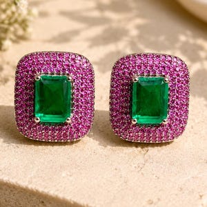 Puede incluir: Un par de pendientes de botón con una piedra central verde de corte esmeralda rodeada por un borde rectangular de pequeñas piedras pavé de color rosa vibrante en un marco de metal plateado, creando un contraste marcado entre los colores.