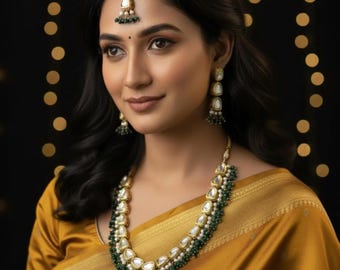 May include: A gold-toned necklace, matching drop earrings, and a maang tikka headpiece featuring white teardrop stones framed in gold, accented with small green beads. The jewelry set is worn with a mustard yellow garment with a gold border.