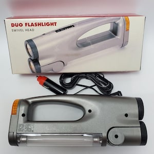 Könnte beinhalten: Graue Duo-Taschenlampe mit Schwenkkopf, Griff und zwei Lichtquellen. Die Box zeigt den Produktnamen. Inklusive Auto-Adapter und schwarzem Kabel.
