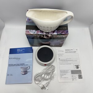 K&ouml;nnte beinhalten: Ein elektrisches So&szlig;enw&auml;rmer-Set bestehend aus einer wei&szlig;en Keramik-Sauciere, einer runden schwarz-wei&szlig;en Heizbasis, einem Netzkabel, einer Bedienungsanleitung und einer Garantiekarte, verpackt in einem Karton mit der Aufschrift Kitchen Living.