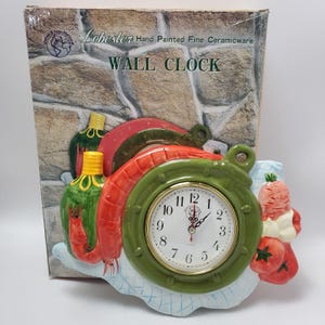 May include: A ceramic wall clock with a green, red, and white design. The clock face is white with black numbers and gold trim. The clock is decorated with painted vegetables and a lobster.
