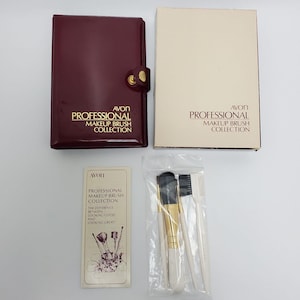 Op de afbeelding: Een Avon Professional Makeup Brush Collection. De afbeelding toont een bordeauxrode etui, een beige doos, een kaart met tekst en een verzegelde zak met penselen. De tekst luidt 'Professional Makeup Brush Collection'.