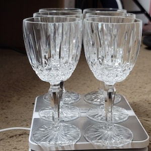 May include: Set of six clear crystal wine glasses. Each glass features a detailed, cut-glass design on the bowl and stem. The glasses are arranged on a scale, showcasing their elegant craftsmanship and clarity. Ideal for formal dining or special occasions.