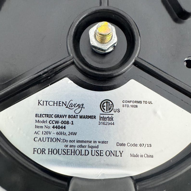 K&ouml;nnte beinhalten: Die Unterseite eines schwarzen elektrischen So&szlig;enw&auml;rmers von Kitchen Living mit einem silbernen Etikett. Das Etikett zeigt das Modell CCW-008-1, Artikel 44044, 120V 60Hz 24W, Intertek ETL-Zertifizierung und den Warnhinweis: Nicht in Wasser tauchen.