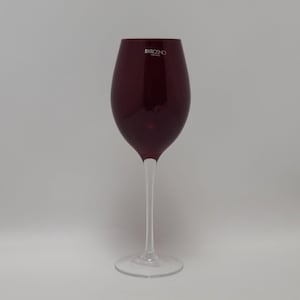 May include: A tall, burgundy-colored wine glass with a long, slender stem and a clear, circular base. The glass has a rounded bowl and the brand name "KROSNO" is printed on the upper part of the glass. The glass is designed for serving wine.