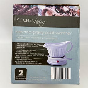 K&ouml;nnte beinhalten: Eine Produktverpackung f&uuml;r einen elektrischen So&szlig;enw&auml;rmer von Kitchen Living. Die Box zeigt eine hellviolette So&szlig;enschale auf einem passenden Sockel mit roter Kontrollleuchte. Der Text enth&auml;lt Produktname, Funktionen und ein 2-Jahres-Garantiesymbol.