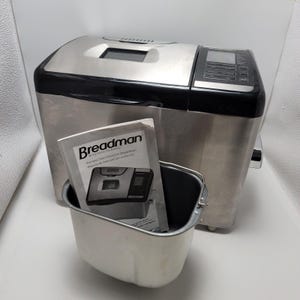 Puede incluir: Una panificadora de convección Breadman de acero inoxidable con tapa y panel de control de plástico negro. Incluye un molde de metal extraíble para pan y un manual de instrucciones impreso con el logotipo de Breadman.