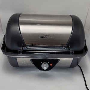 May include: A Crock-Pot BBQ PIT electric grill with a brushed stainless steel lid and black plastic housing. The front features a central control knob with Off, Low, and High settings, a red indicator light, and a black horizontal handle.