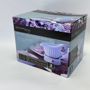 K&ouml;nnte beinhalten: Ein rechteckiger Karton f&uuml;r einen elektrischen So&szlig;enw&auml;rmer von Kitchen Living. Die Verpackung zeigt eine hellviolette So&szlig;enschale auf einem Sockel mit dem Text "electric gravy boat warmer", "calentador electrico para salsera" und "2 year warranty".
