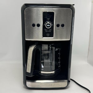 May include: A black and silver Krups coffee maker with a glass carafe. The front panel features a digital display, a central brew dial, and buttons labeled Auto On, Reg Bold, 1-4 Cups, Clean, Temp, Time, Keep Warm, and Turbo. The carafe has cup markings.