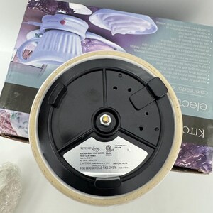 K&ouml;nnte beinhalten: Die Unterseite eines elektrischen So&szlig;enw&auml;rmers von Kitchen Living, Modell CCW-008-1, mit einem schwarzen runden Boden, drei schwarzen Standf&uuml;&szlig;en, einem zentralen Metallkontaktpunkt und einem silbernen Etikett mit elektrischen Angaben.
