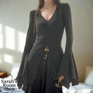 May include: Black long-sleeved top with a V-neck and flared sleeves. The top has a front slit with a buckle fastening. The sleeves have a ruffled edge. The Sarah's Room Shop logo is in the bottom left corner.