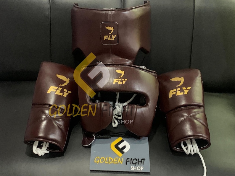 May include: A set of boxing equipment in a dark brown color. The set includes a head guard, a chest protector, and two boxing gloves. Each piece has the word "FLY" and a logo printed on it. A sign that says "GOLDEN FIGHT SHOP" is at the bottom.