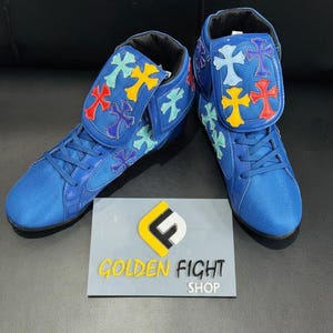 Puede incluir: Zapatillas altas azules con diseños de cruces coloridas en la lengüeta y los laterales. Las zapatillas tienen cordones azules y una puntera de malla. Los zapatos se exhiben sobre una superficie gris con un letrero que dice "GOLDEN FIGHT SHOP".