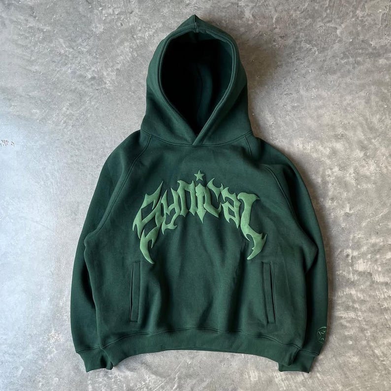 Puede incluir: Sudadera con capucha verde oscuro con capucha y bolsillo delantero. La palabra "Cynical" est&aacute; bordada en el pecho con una fuente estilizada en verde claro. La sudadera est&aacute; hecha de un material suave.