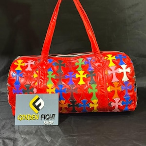 Könnte beinhalten: Eine rote Leder-Reisetasche mit einem bunten Kreuzmuster. Die Tasche hat zwei rote Griffe und einen silbernen Reißverschluss. Die Tasche wird von einer Hand gehalten. Der Text "GOLDEN FIGHT SHOP" steht auf einem grauen Schild.