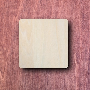 May include: A square, light-coloured wooden coaster with rounded corners. It sits on a dark reddish-brown wooden surface, creating a contrast in tones. The coaster appears to be made of natural wood.