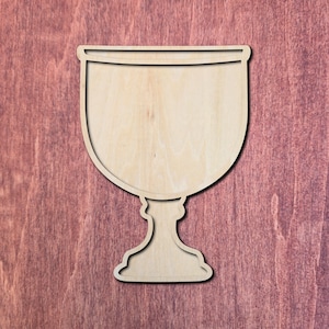 May include: A wooden chalice cutout, featuring a wide bowl and a detailed stem. The chalice is made of light-colored wood, with visible grain, and is set against a reddish-brown wooden background. The cutout has a shadow effect.