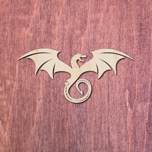 May include: A wooden dragon cutout with outstretched wings and a curled tail. The dragon is light-coloured, possibly unfinished wood, and is set against a reddish-brown background. The dragon's design includes detailed wing and body features.