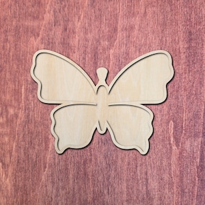 May include: A flat, light-colored wooden cutout in the shape of a butterfly. The butterfly features a symmetrical design with two large upper wings and two smaller lower wings, all connected by a central body section with a small head detail.