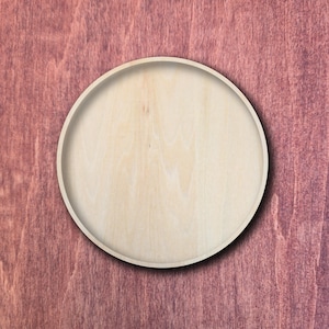 May include: A circular wooden tray with a light beige, natural wood grain finish and a raised rim. The tray features a smooth, flat surface and a consistent, pale wood tone throughout, showcasing the organic texture of the wood material.