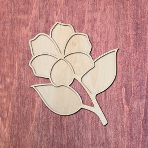 May include: A wooden flower cutout with petals and leaves. The flower is made of light-colored wood and has a detailed outline. The background is a reddish-brown wood grain.