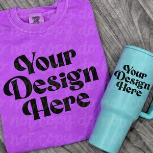 May include: A purple t-shirt and a teal tumbler with the text "Your Design Here" in a bold, black font. The t-shirt has a crew neck and a small tag. The tumbler has a handle.