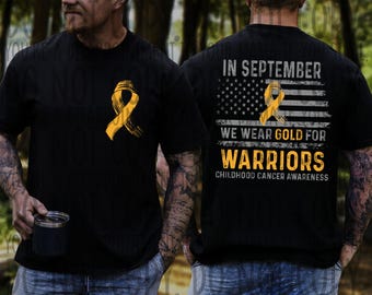 May include: Black t-shirt with a gold ribbon graphic on the front and back. The back of the shirt features an American flag design with the text "IN SEPTEMBER WE WEAR GOLD FOR WARRIORS CHILDHOOD CANCER AWARENESS."