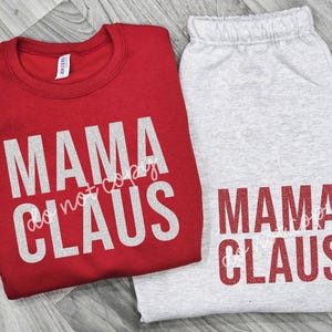 May include: A red crew neck sweatshirt and gray sweatpants set. The sweatshirt and sweatpants both feature the text "MAMA CLAUS" in a glittery, silver font. The sweatshirt has a tag on the upper left side. The text "do not copy" is also visible.