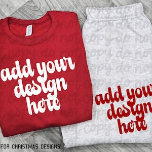 May include: A red crew neck sweatshirt and gray sweatpants set. Both items feature the text "add your design here" in a white and red script font, respectively. The set is designed for custom Christmas designs.
