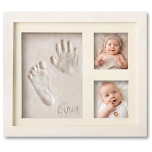 May include: A white framed baby keepsake with a foot and handprint, two baby photos, and the name "LIAM" inscribed. The frame has a cream-colored matting.