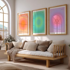 Puede incluir: Tres impresiones art&iacute;sticas enmarcadas con dise&ntilde;os abstractos en tonos naranja, verde y morado cuelgan sobre un sof&aacute; de madera con cojines de colores neutros y una manta. La habitaci&oacute;n tiene una gran ventana arqueada.