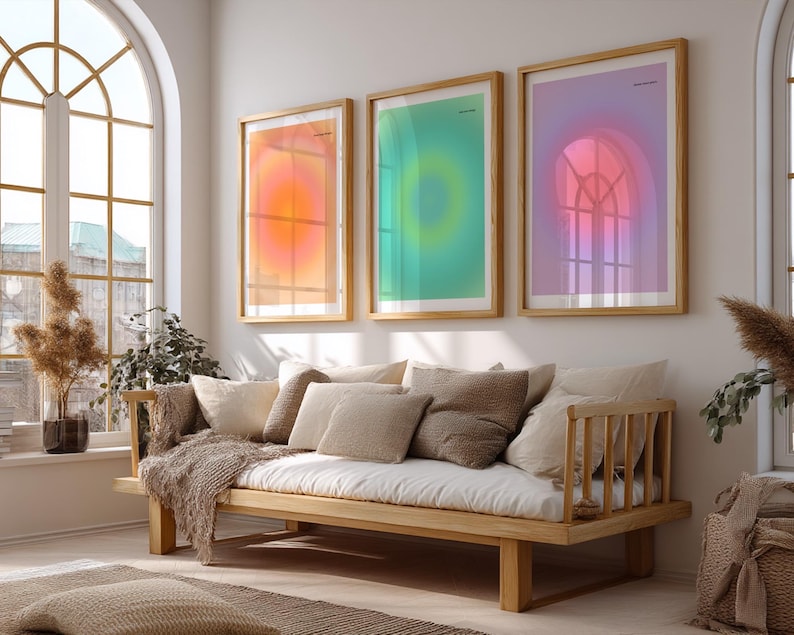 Puede incluir: Tres impresiones art&iacute;sticas enmarcadas con dise&ntilde;os abstractos en tonos naranja, verde y morado cuelgan sobre un sof&aacute; de madera con cojines de colores neutros y una manta. La habitaci&oacute;n tiene una gran ventana arqueada.