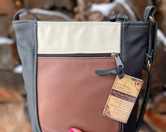 May include: A brown, black, and white leather crossbody purse with a zipper closure. The purse has a tag attached that reads "The Purse Peddlers" and includes the company's contact information.
