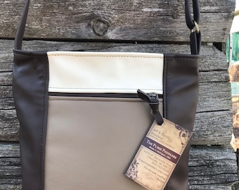 May include: A brown, tan, and cream-colored leather crossbody bag with a long strap. The bag has a zippered top and a tag that reads "THE PURSE PEDDLERS". The bag is made of leather and has a simple, classic design.