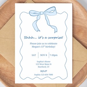 May include: A white invitation card with a light blue bow illustration and text. The text reads "Shhh... it's a surprise!" and invites guests to Megan's 13th birthday on November 8th. Includes RSVP information.