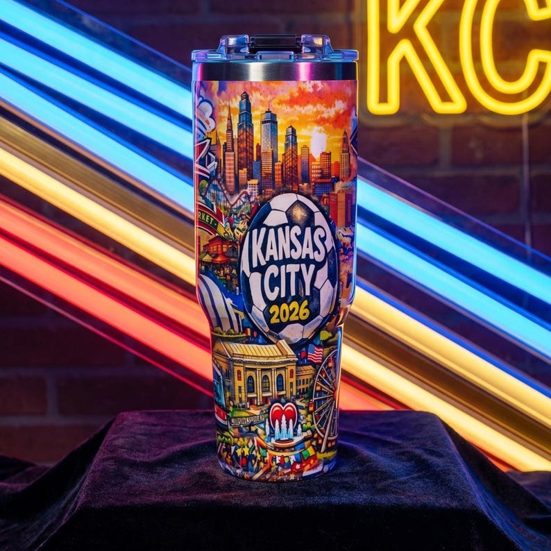May include: A stainless steel tumbler featuring a colorful design of the Kansas City skyline, a soccer ball, and the text "Kansas City 2026." The design includes a sunset, buildings, and other city landmarks.
