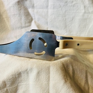 May include: A vintage cake server with a stainless steel blade and a cream-coloured plastic handle. The blade has a decorative cutout design. The server is designed to lift and serve slices of cake or pie.