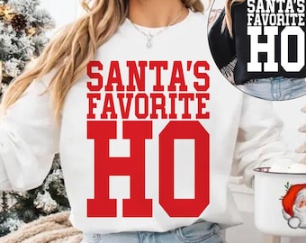 May include: White sweatshirt with the text "SANTA'S FAVORITE HO" in red block letters. The image also shows a black sweatshirt with the same text. A Christmas tree and a Santa mug are also visible.