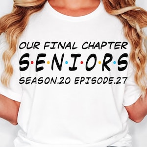 May include: A white short-sleeved t-shirt featuring the black text 'OUR FINAL CHAPTER' at the top, 'S E N I O R S' in the middle with small colored dots between letters, and 'SEASON.20 EPISODE.27' at the bottom, paired with blue denim jeans.